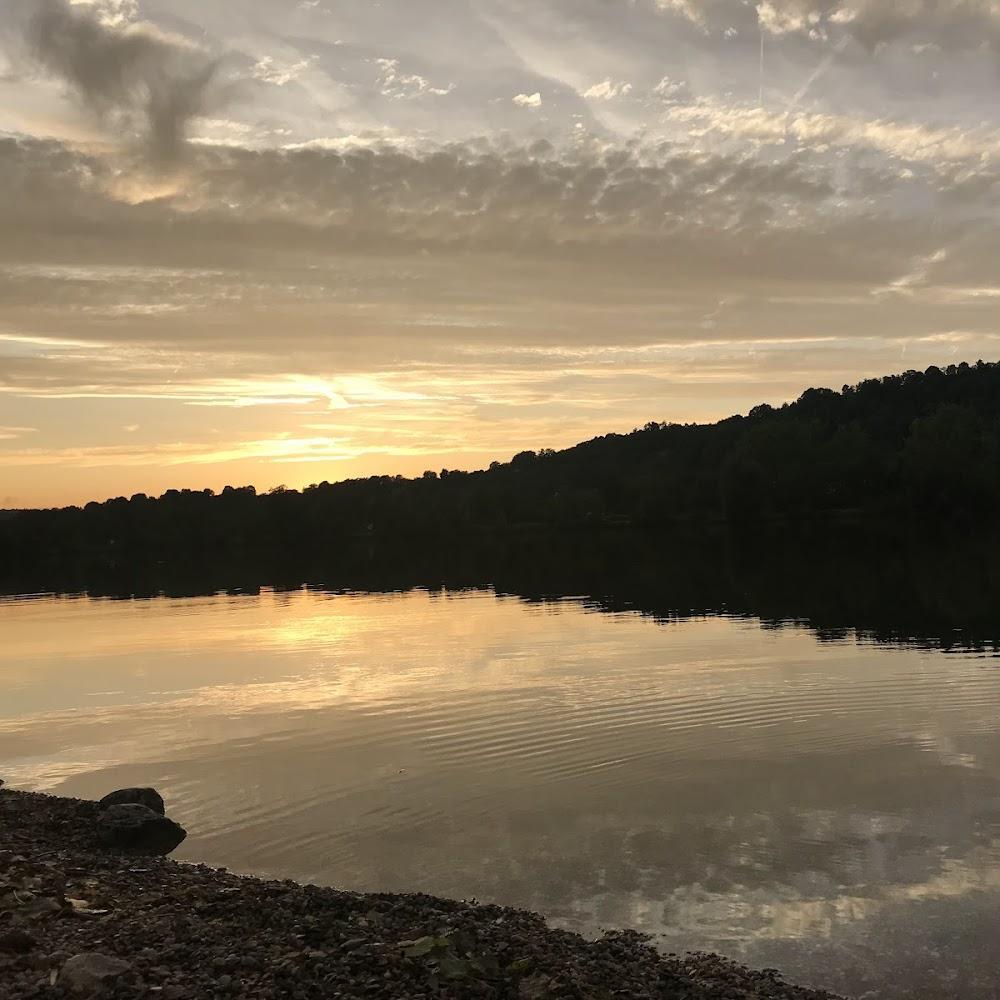 A calm lake with cloudy sunset and a pebbled shore.